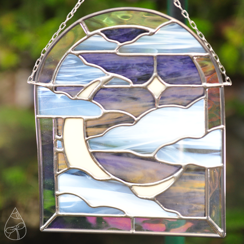 A stained glass suncatcher of a Moonlit Window - featuring a crescent moon, star, and clouds framed in an arched window. 
